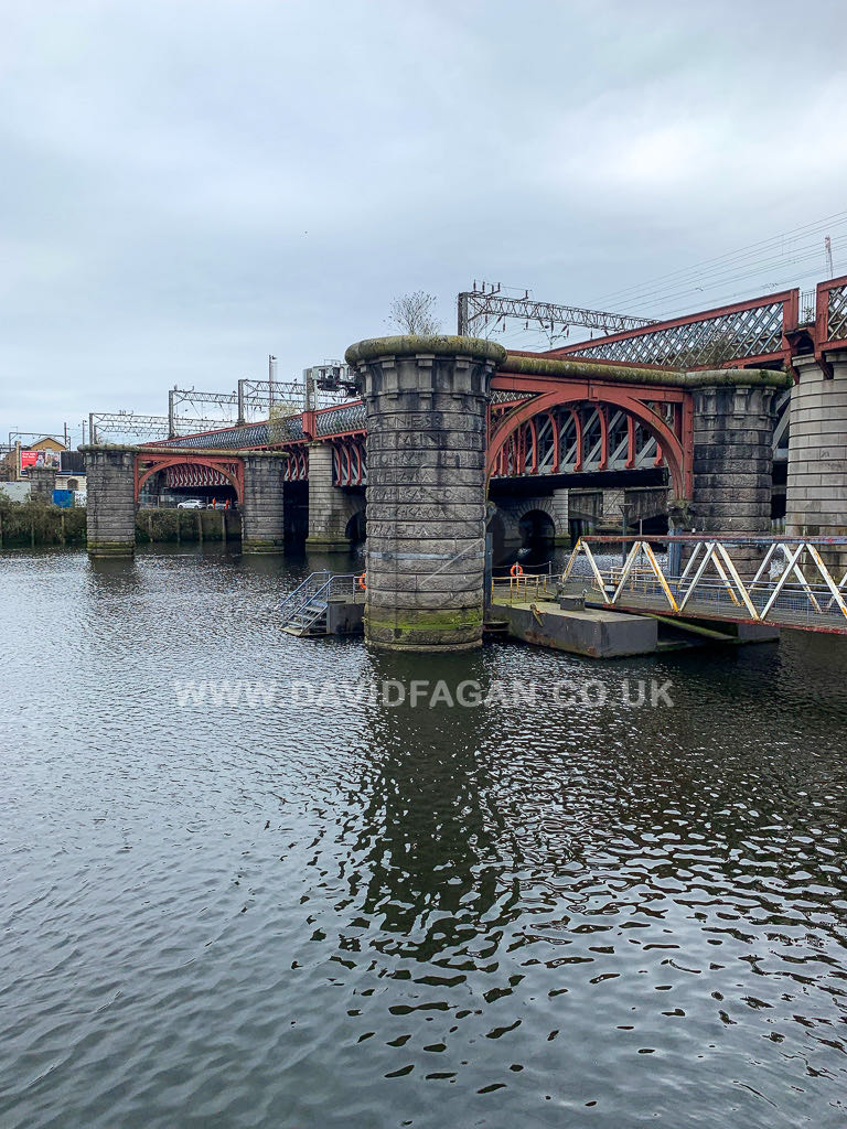 Stone piers and red steelwork of a railway bridge crossing the river
