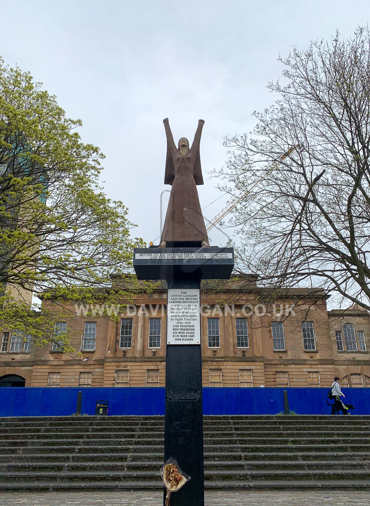 A bronze statue of a woman with raised arms on a tall plinth beside the River Clyde in Glasgow