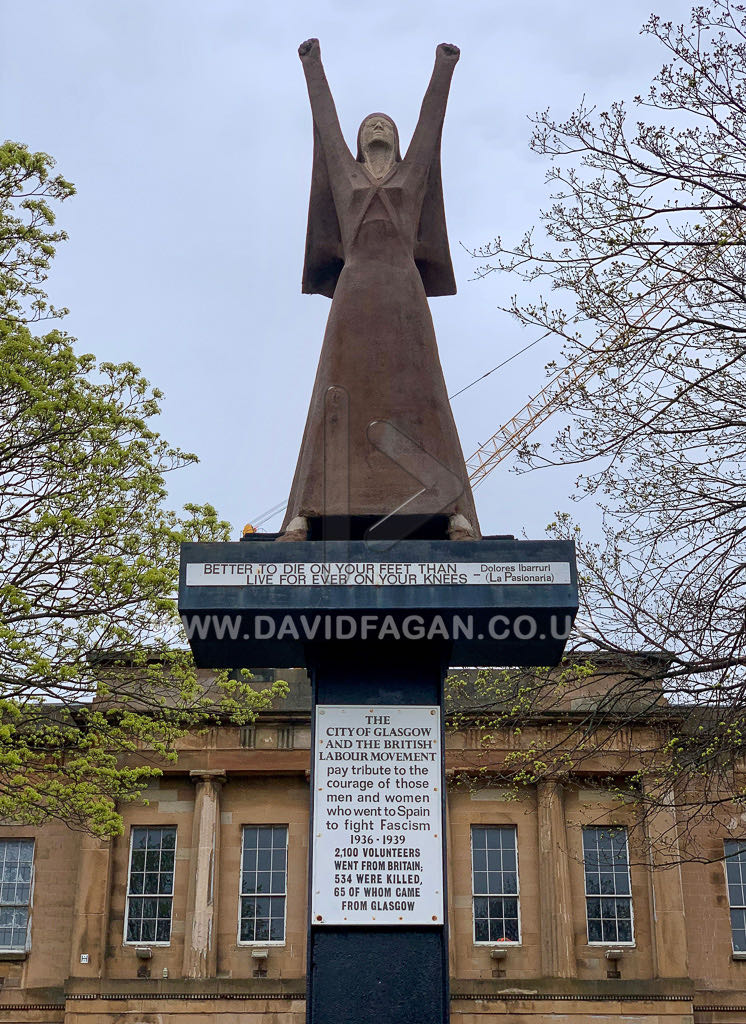 The same riverside statue seen from behind, with a construction crane across the water